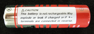 A photograph shows a warning label on the side of a consumer dry cell. The label reads “Caution. This battery is not rechargeable. May explode or leak if charged of if positive and negative terminals are connected in reverse.”