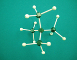 A photograph shows a molecular model for 2,2 –dimethylpropane, a form of C5H12. Black balls represent carbon atoms and white balls represent hydrogen atoms. All bonds between balls are a single connection. The model has three black balls joined together to form a chain. Three white balls are joined to the first and third black balls in the chain. The second black ball in the chain is also attached to two black balls, each having three white balls attached. 