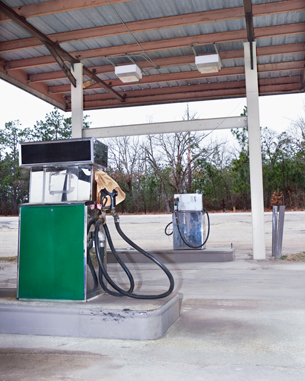 A photograph shows two green gasoline pumps at an abandoned gasoline station.