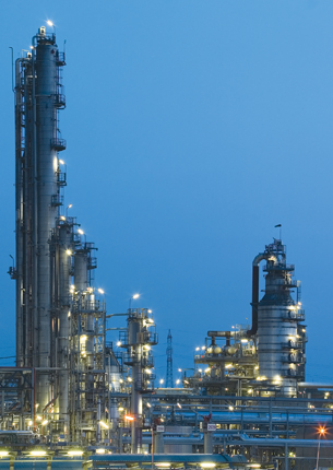 A photograph shows a brightly lit chemical plant at dusk.