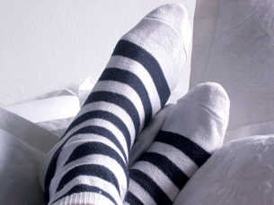 A photograph shows two feet wearing white socks with black stripes. The feet are crossed and resting on couch cushions. 