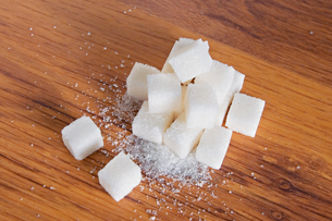 A photograph shows white sugar cubes piled on a brown table. Some of the cubes have crumbled and white crystals are at the base of the cubes.