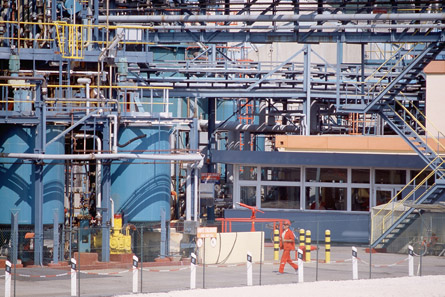 A photograph shows the inside of a chemical factory and the many large cylinders and vessels held within a network of scaffolding.