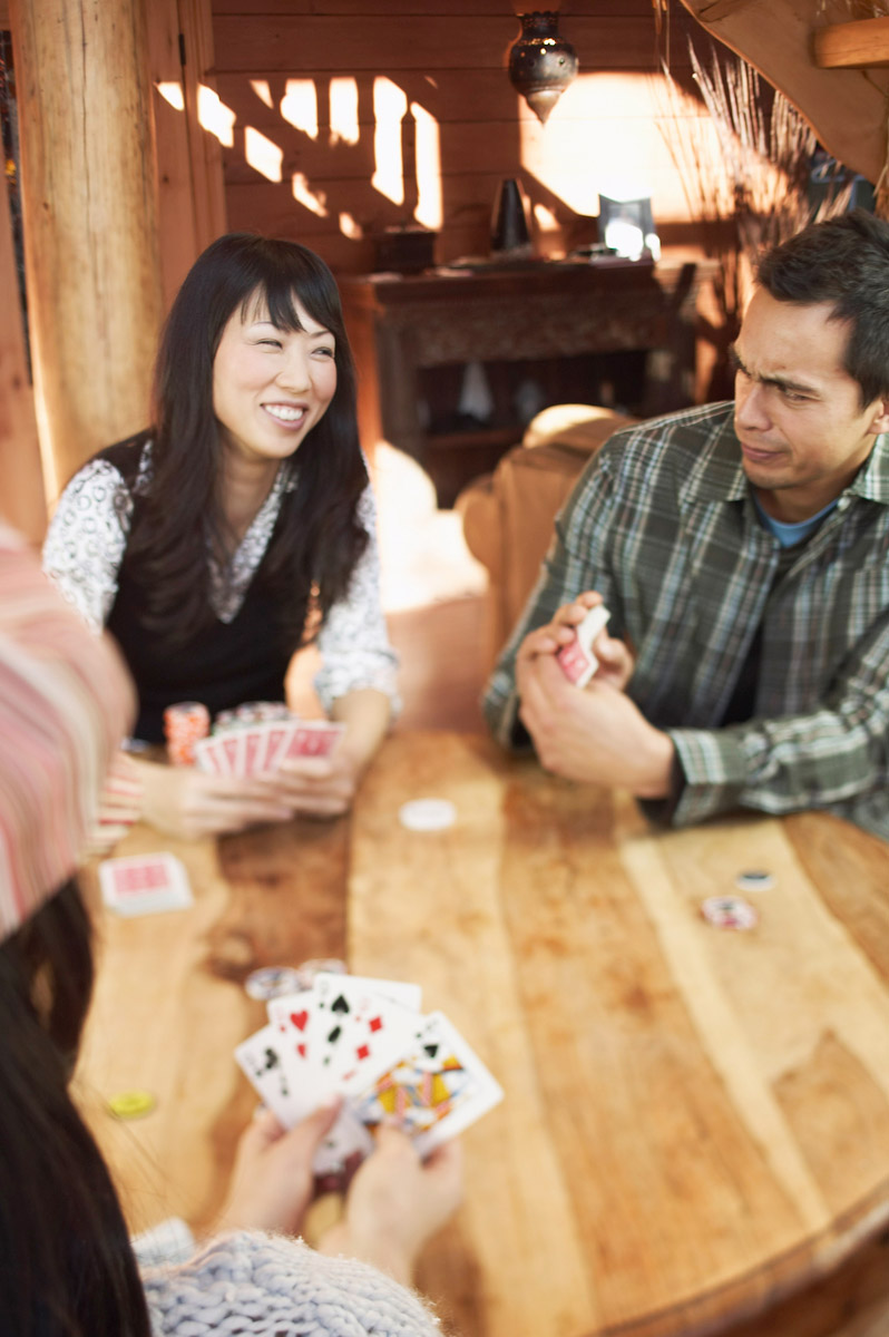 A photograph shows three people playing a card game inside a log cabin. 