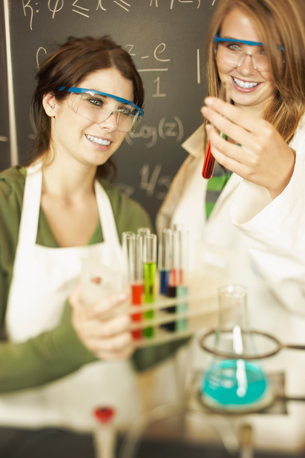 A photograph shows two female students in a chemistry lab examining tubes containing solutions in a variety of colours.