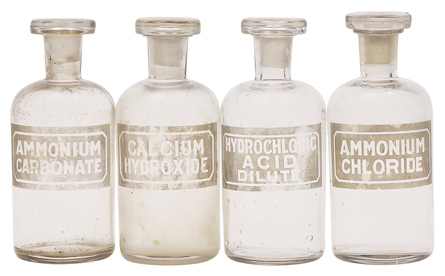 A photograph shows four colourless glass bottles. The labels on the bottles are: ammonium carbonate, calcium hydroxide, hydrochloric acid dilute, and ammonium chloride.