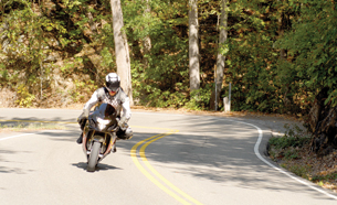 Motorcyclist negotiating turns on a country road. The motorcyclist in this photo is wearing a full-face helmet and driving a sport bike. 