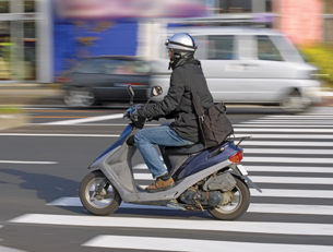 The photo shows a person on a motorized scooter in city traffic. 