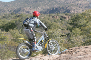 The photo shows a person wearing a helmet while riding a dirt bike over a rocky area. 