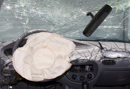 This photo is a view from the driver’s seat of a wrecked car. The photo shows the shattered windshield and the driver’s airbag deployed.