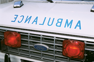 The photograph shows the front of an ambulance, with the word “ambulance” spelled backwards to be read by drivers in their rearview mirrors.