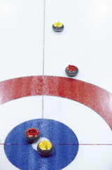 A photo shows four curling stones, two yellow and two red, on a curling rink. A red and a yellow stone are on the button (centre of the target); the other stones sit outside the house (the rings that comprise the target), with the red stone closest to the outer ring.