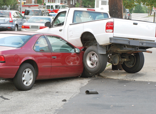 The photograph shows a collision between a red car and a white pickup truck. The truck is on the hood of the car.