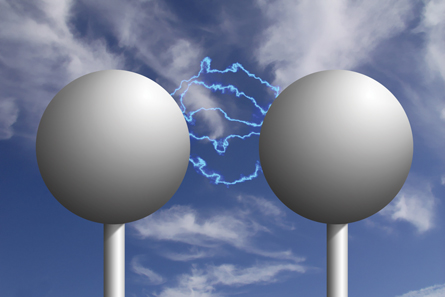 Two large metal spheres are shown with electric discharge streamers arcing from one sphere to the other.