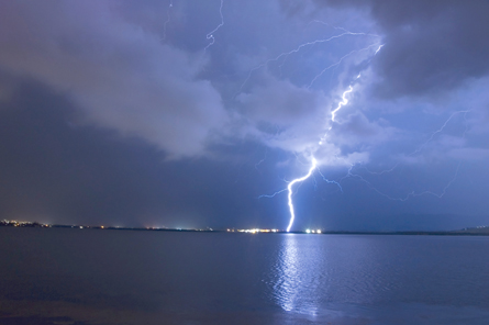 A single bolt of lightning is shown striking a settlement on the distant shore of a large lake.