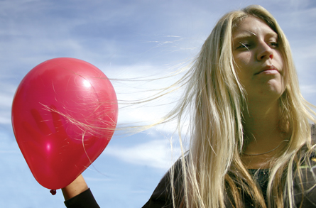 The photo shows a young woman holding a red balloon. The young woman’s hair is attracted to the balloon.