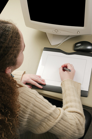 The photo shows a young woman working with a graphics tablet in front of a computer monitor. 