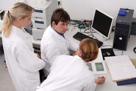 The photo shows a team of 3 researchers having a discussion in front of a computer monitor. 