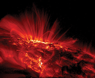 An image shows a close-up of a sunspot arc on the surface of the sun in ultraviolet light, taken by the TRACE spacecraft. It appears red, with streamers rising out of a glowing field on the sun’s surface.