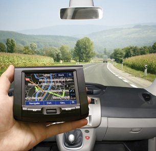 A photograph shows the hand of someone holding a GPS receiver in a vehicle. 