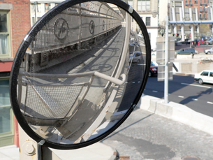 A photograph shows a curved mirror. The reflected image is different than it would be reflected in a flat mirror. Straight lines are distorted.