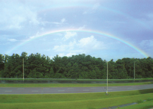 A photo shows a double rainbow arcing over a stand of trees. A rainbow is an optical illusion produced by the refraction of sunlight in water droplets in Earth’s atmosphere.