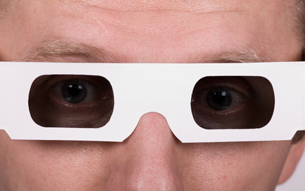A photograph shows a man watching a 3-D movie while wearing polar filter glasses.