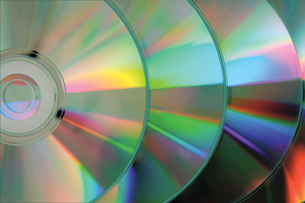 A photo shows the backs of several CDs or DVDs. The discs produce a spectrum when white light is reflected from their grooved surfaces.