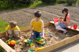 This photo shows three children, two boys and a girl, playing in a sandbox.