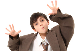 This photo shows a young boy dressed up in a man’s suit jacket, dress shirt, and tie.