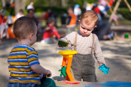 This photo shows two toddler boys playing with sand toys in an outdoor environment.