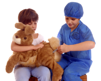 This photograph shows two young children pretending to work in a veterinary clinic. One child is pretending to give an injection to a large stuffed toy rabbit while the other child is holding the rabbit.