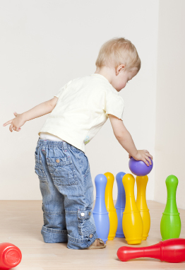 This photo shows a toddler playing with a toy bowling set.