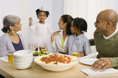 This photo shows a family gathered around the dinner table. The family appears to include a mother and father, a young daughter, a young son, and a grandmother.