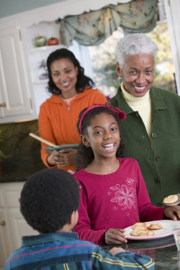 This photo shows two children, a boy and a girl, in a kitchen with two women. One woman has white hair, and appears to be older than the other woman, who might be the mother of the children.