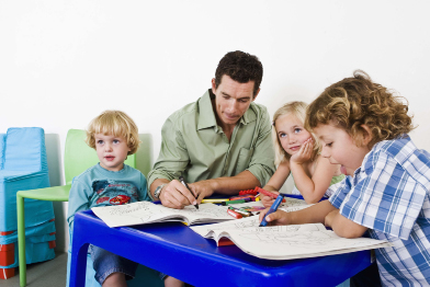 This photo shows a man colouring at a table with three young children.