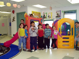 A group of First Nations children is gathered around a play structure in a child care setting.