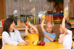 A child care worker and three children are pictured playing a food game.