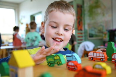 Young children need to play with safe toys. In this photo a young boy is shown playing with blocks that represent cars, trucks, and buses.
