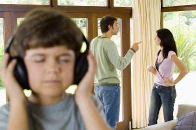 In this photo a child concentrates on listening to his headphones. Meanwhile, a serious discussion takes place behind him.
