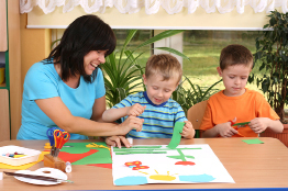 An early childhood professional works on an art project with two children in this photo.