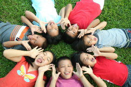 A group of children are lying on their backs on the grass and making faces.