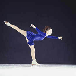 This is a photo of a young woman figure skating with her arms and one of her legs outstretched.