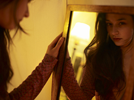 This is a photo of a young woman looking in a large mirror.