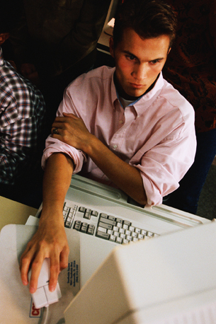 A photograph shows a young man sitting at a computer.