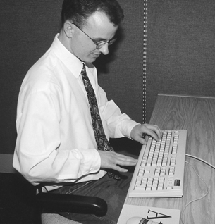 Image of a man sitting at a computer workstation with hand open showing correct distance from abdomen to the edge of the computer desk.