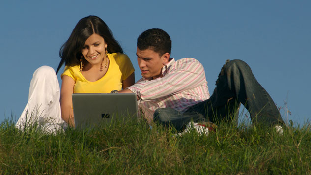 Picture of a young male and female looking at laptop on top of hill.