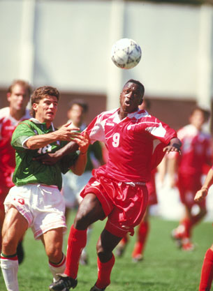 In this photograph, two male soccer players on opposite teams compete for a soccer ball during a game.