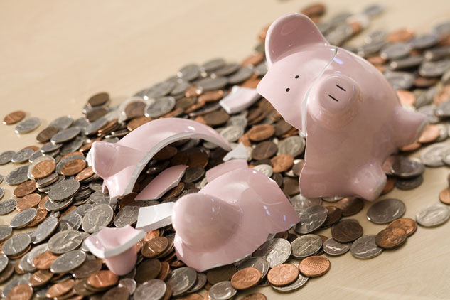 A broken piggy bank with money falling out is seen in this photograph.