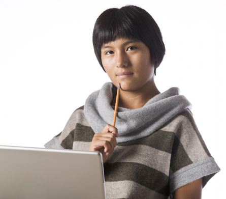 This is a photograph of a young person sitting in front of a laptop computer. The young person has a thoughtful expression.